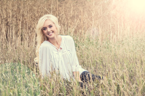blonde high school senior girl sitting in a field of grasses