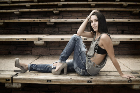 high school senior in jean overalls sitting in concert seating at red rocks