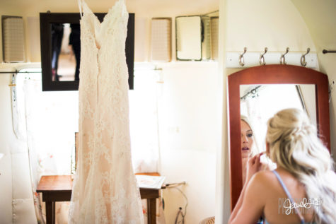 bride doing makeup in a mirrow with her dress hanging next to her