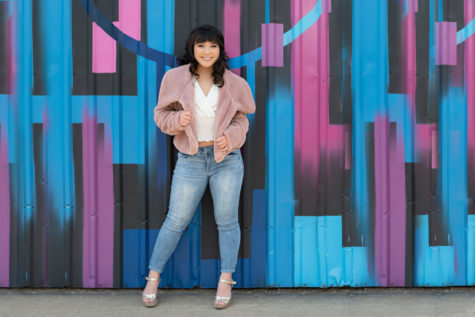 high school senior against a blue, pink, and black mural in a fuzzy pink coat and jeans