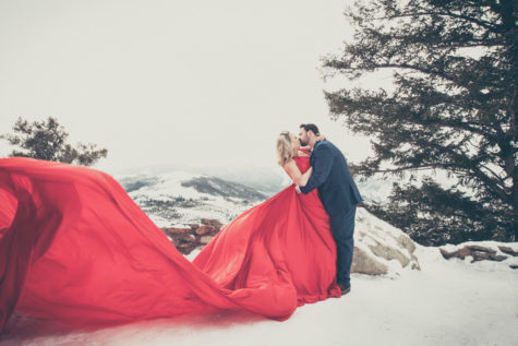 colorado engagement photography of couple kissing wearing a long read dress and blue suit in a snowy setting