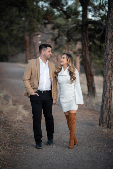 denver engagement photography of couple wearing black, white, and tan walking in the mountains and looking at each other
