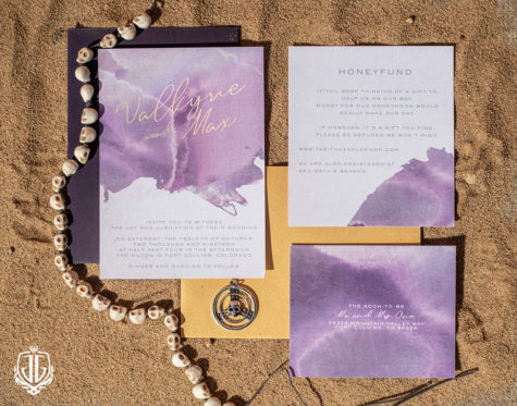 flat lay of invitation suite for a wedding purple and yellow in sand